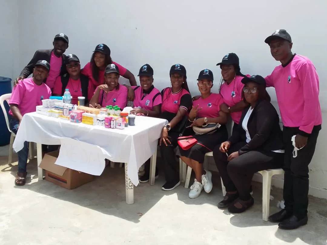 About a dozen members in pink branded shirts and caps gathered around a table of medical supplies