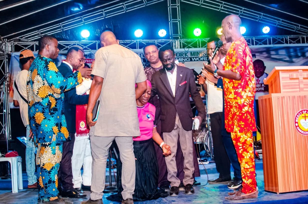 Bishops and pastors gathered around the Convener on stage with hands laid in prayer