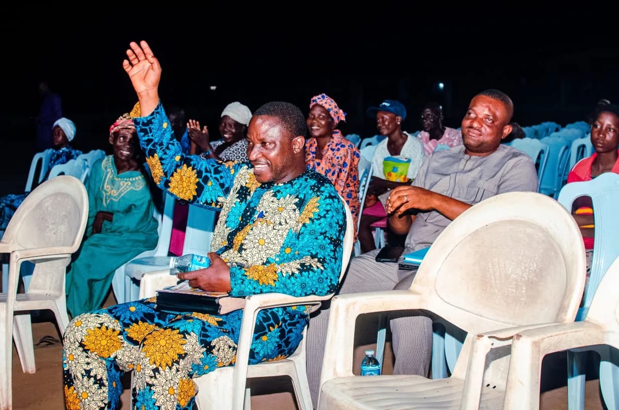 A man in blue and gold Ankara raising his hand among seated attendees at the night crusade
