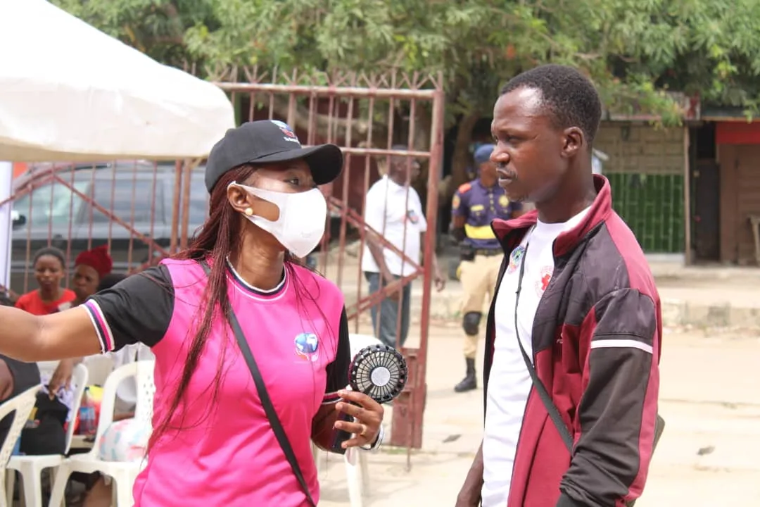 The Convener in a pink branded shirt and face mask speaking with a Red Cross volunteer