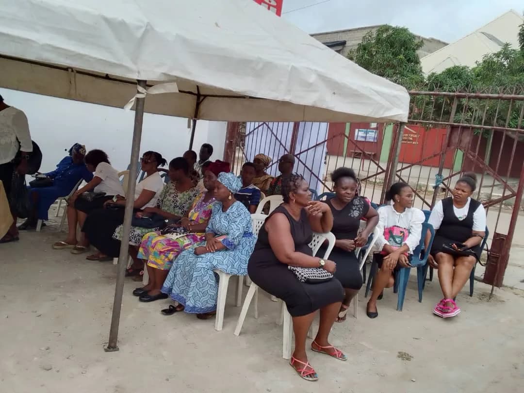 Residents waiting seated under a white canopy in the compound