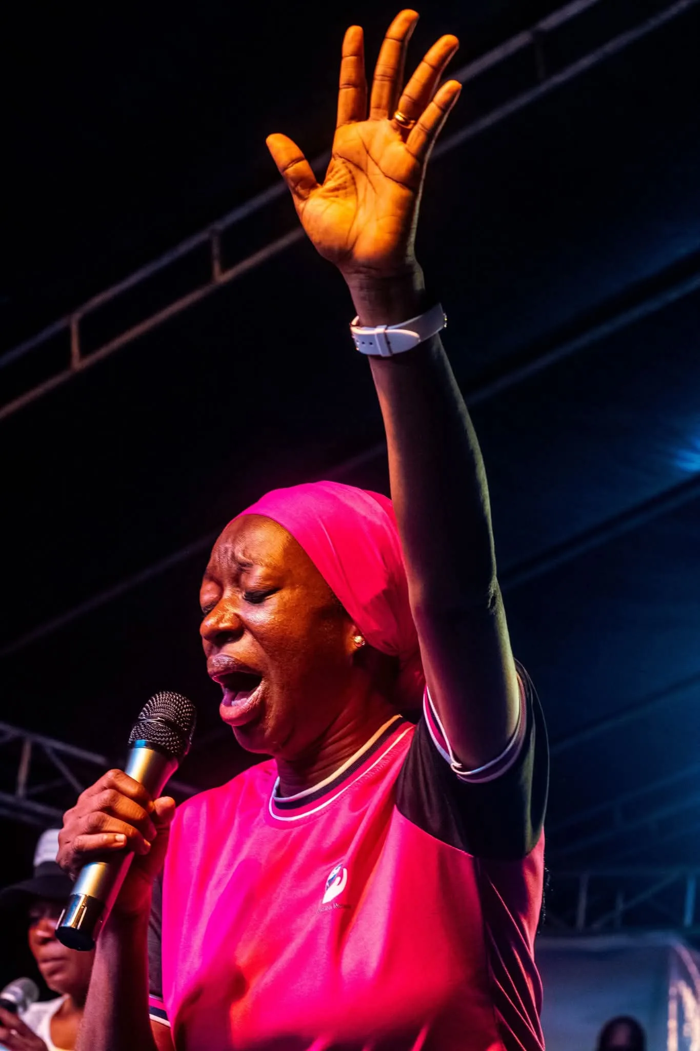 A worshipper singing with one hand raised under stage lighting